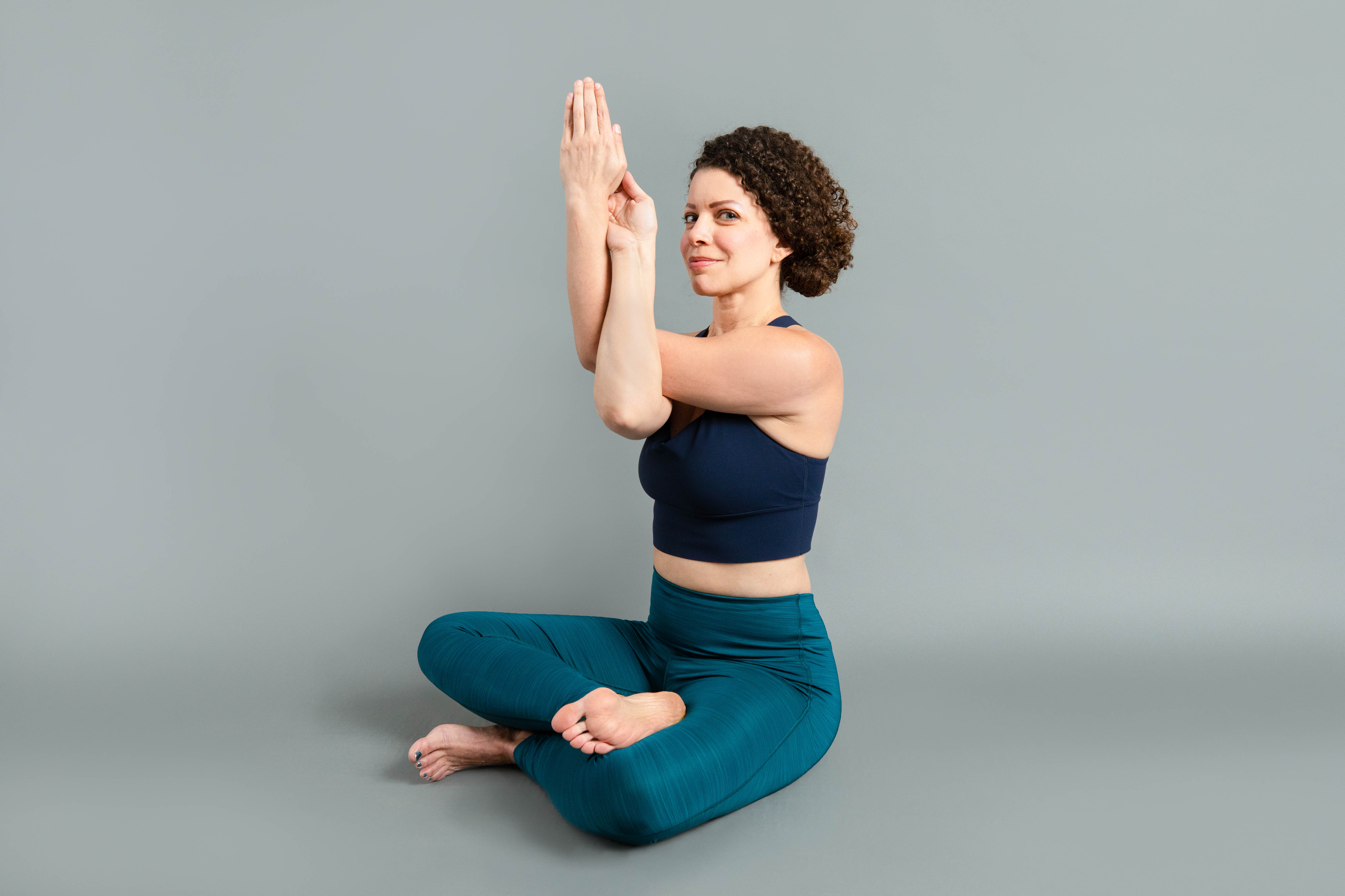 Yoga student sitting cross legged and arms intertwined in front of her