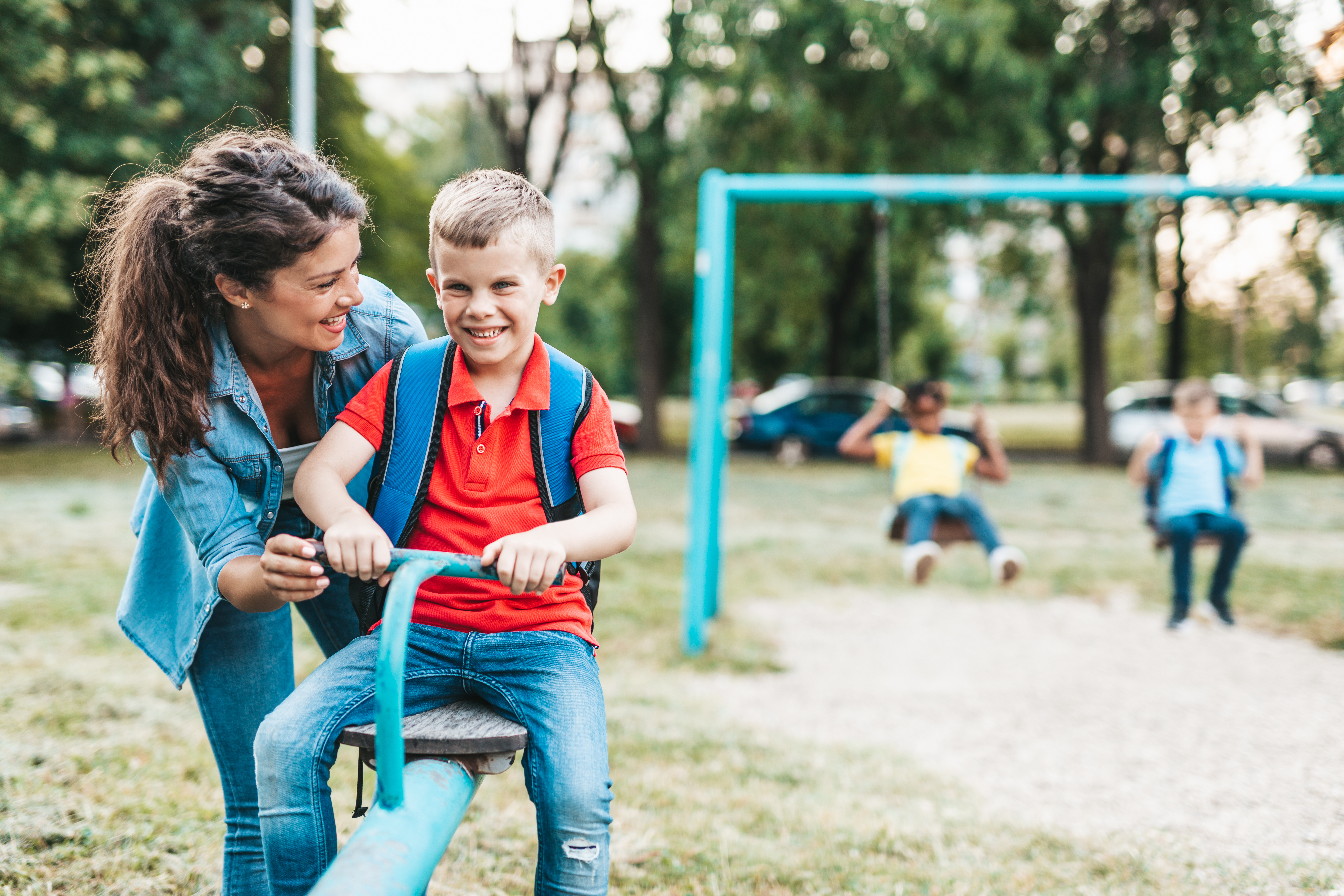 child in a seesaw with an adult standing next to child