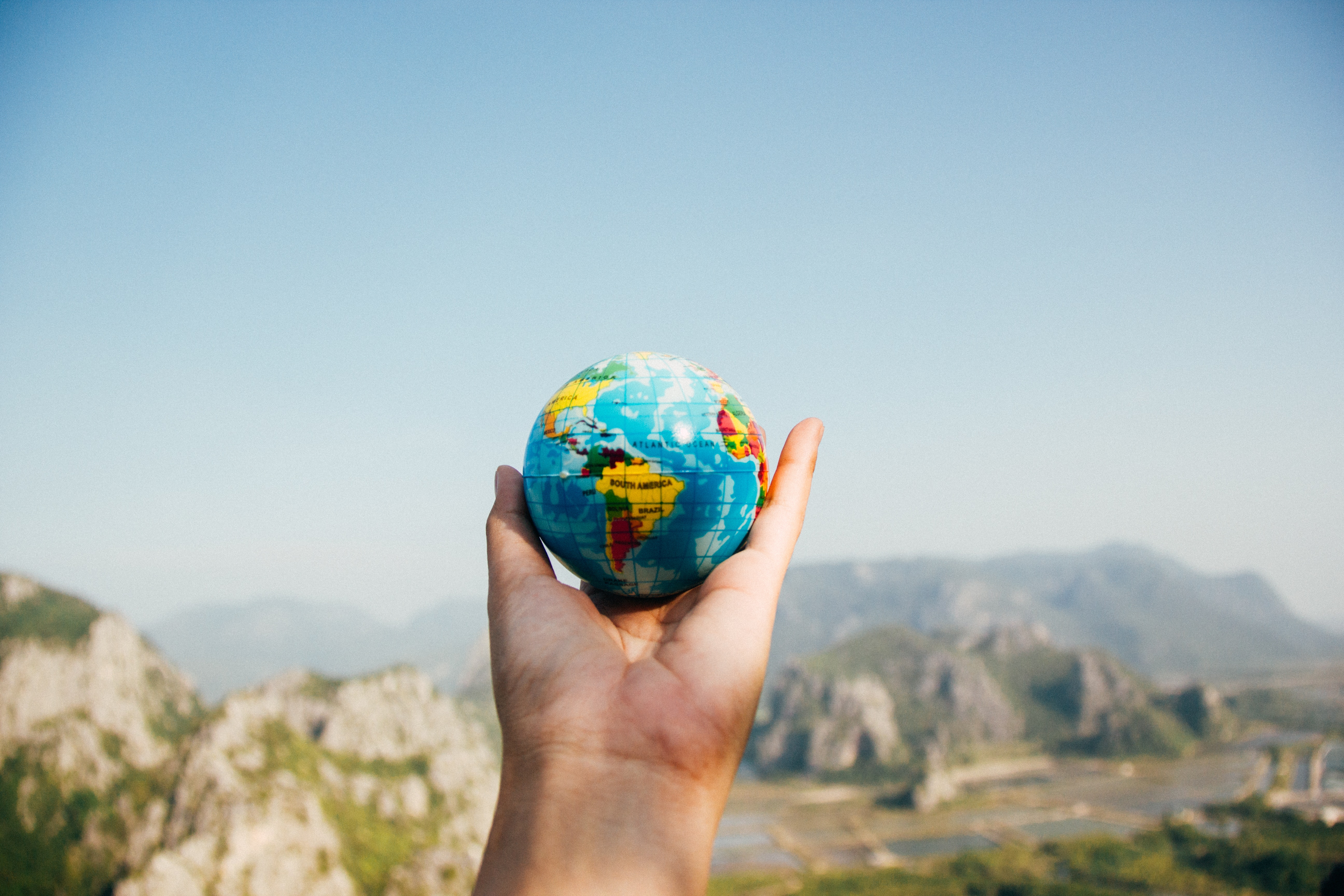 hand holding up small globe in the sky