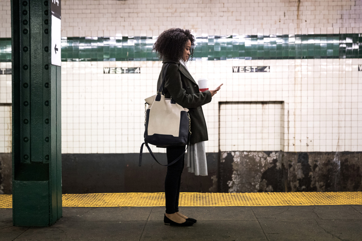 Woman waiting in subway station looking down at her cellphone