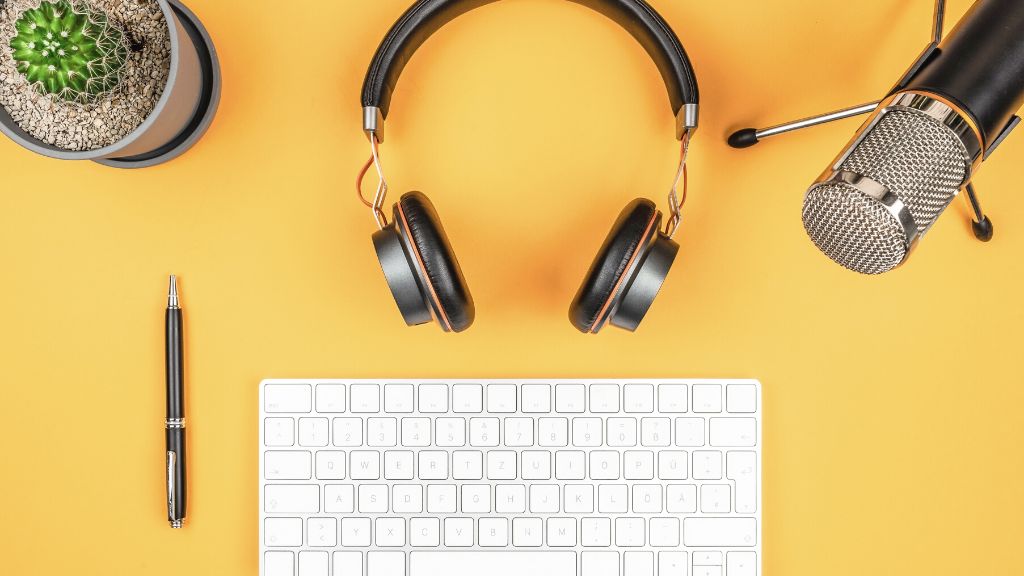 Headphones, podcast microphone, keyboard, pen, and plant on a yellow desk