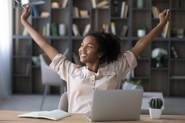 Sitting at a computer woman stretching her arms up above head and smiling