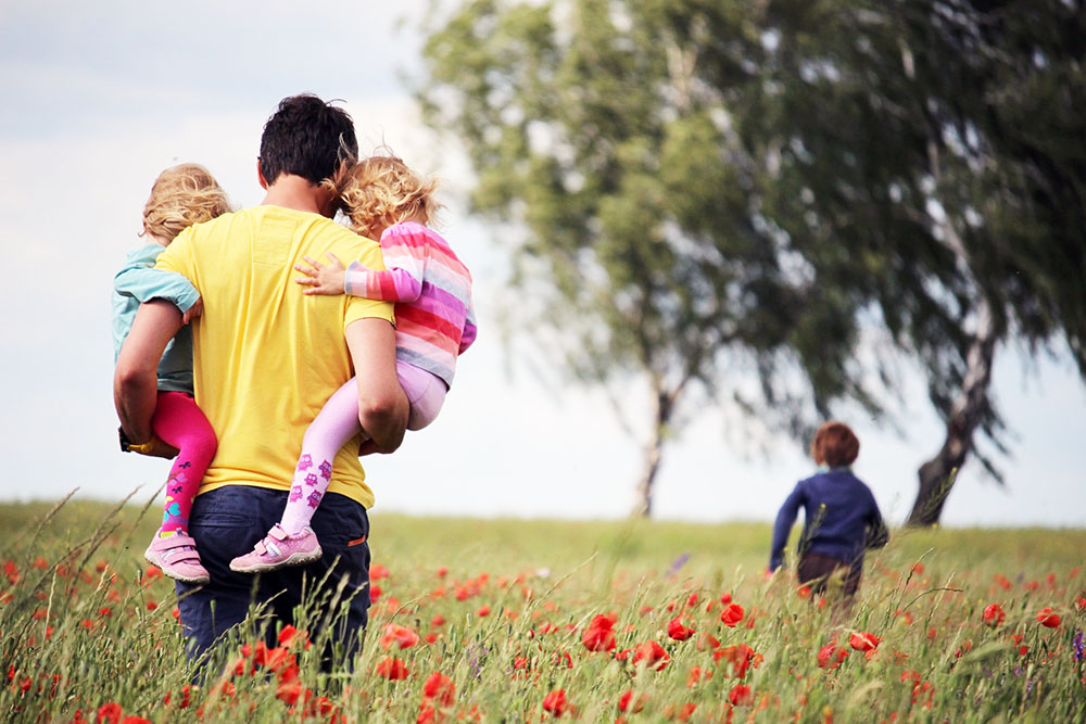 Young man carrying children in meadow