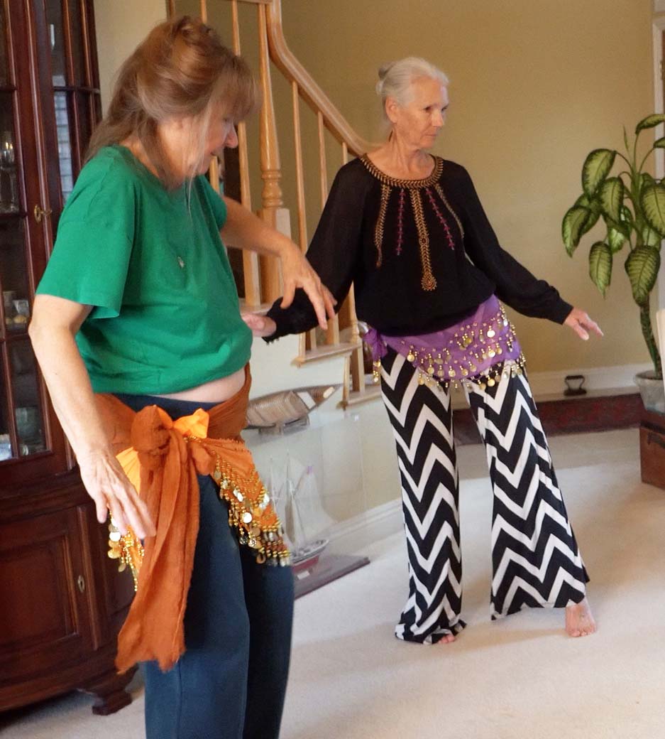 mature senior women wearing hip scarfs learning to belly dance in living room