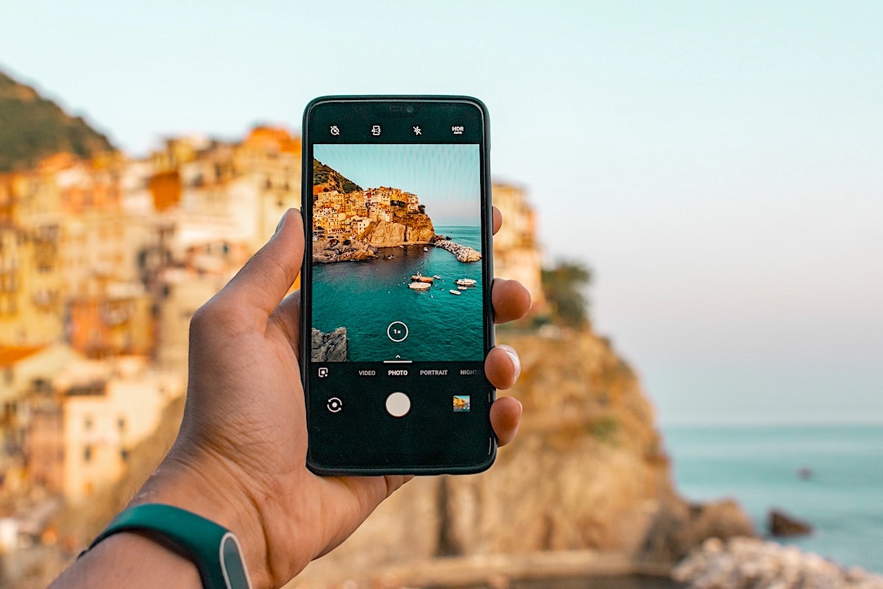 Person holding a smartphone whilst taking a photo of a hillside town by the sea