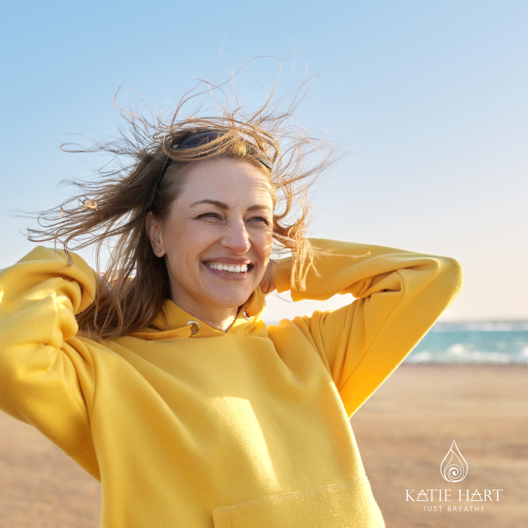 really happy woman smiling on a beach. She has conquered her anxiety. She is wearing a yellow jumper. She is around 40 - 50 years old.