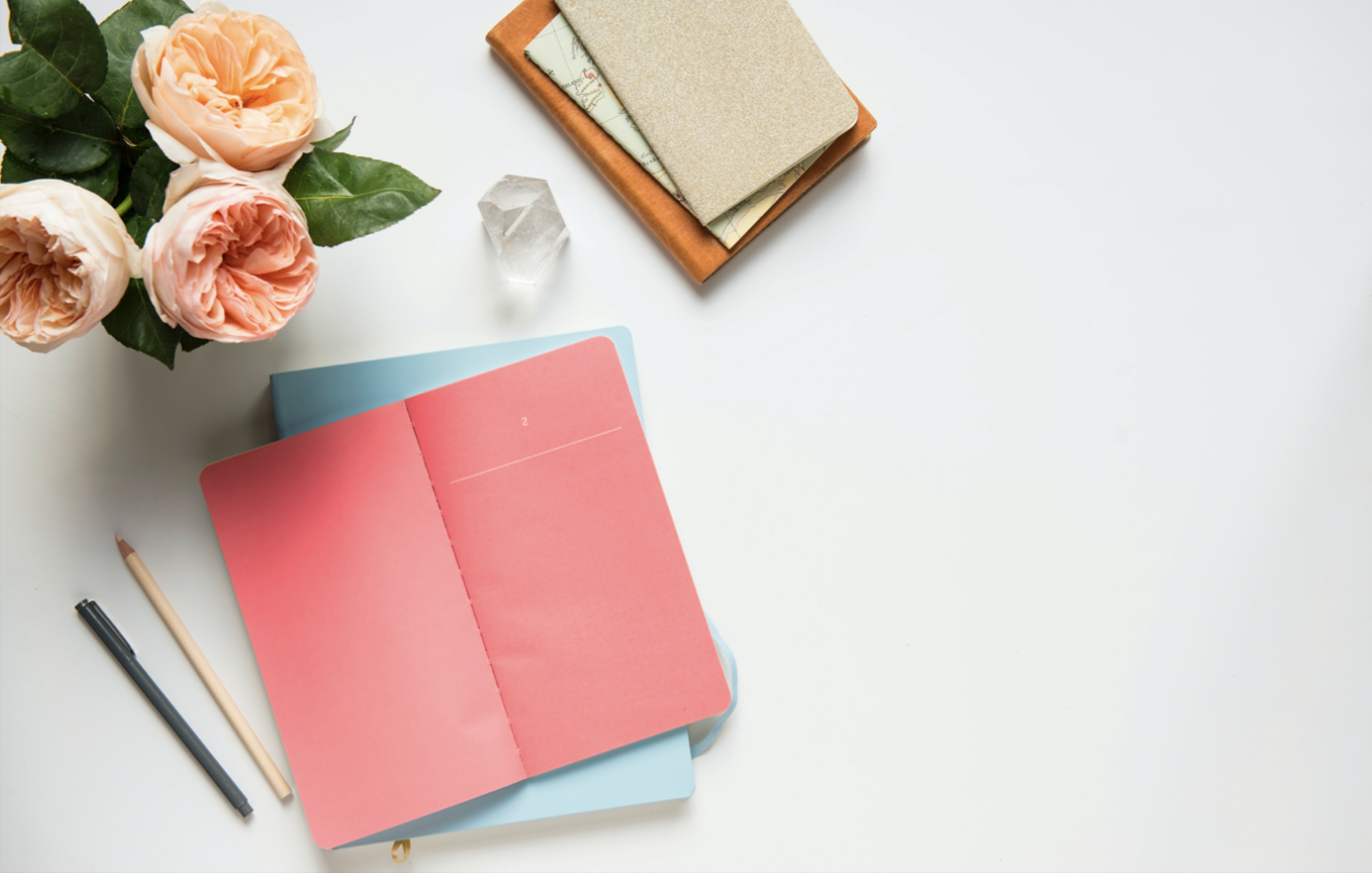 Top-down view of colorful notebooks and a vase of peonies on a light-gray desk