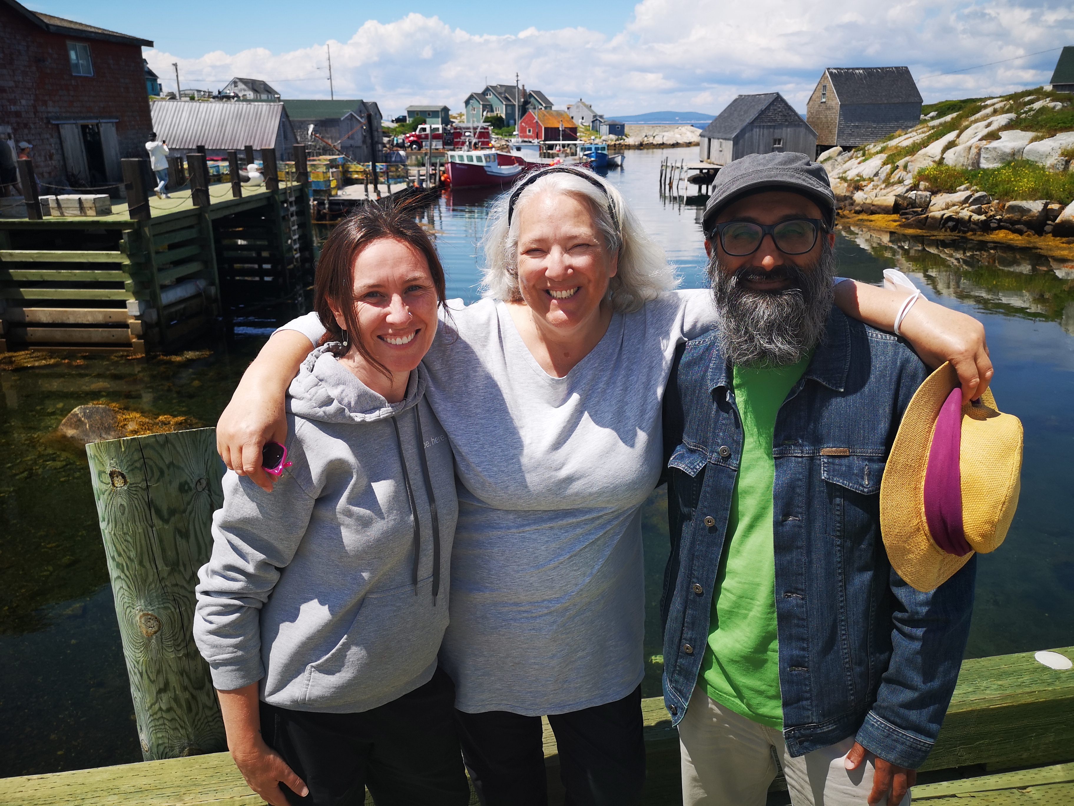 3 happy people stand together in front of a fishing village at Peggy&#39;s Cove in Nova Scotia, Canada