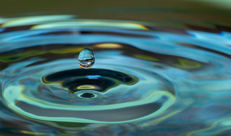 Blue green colored drop of water into a puddle of water