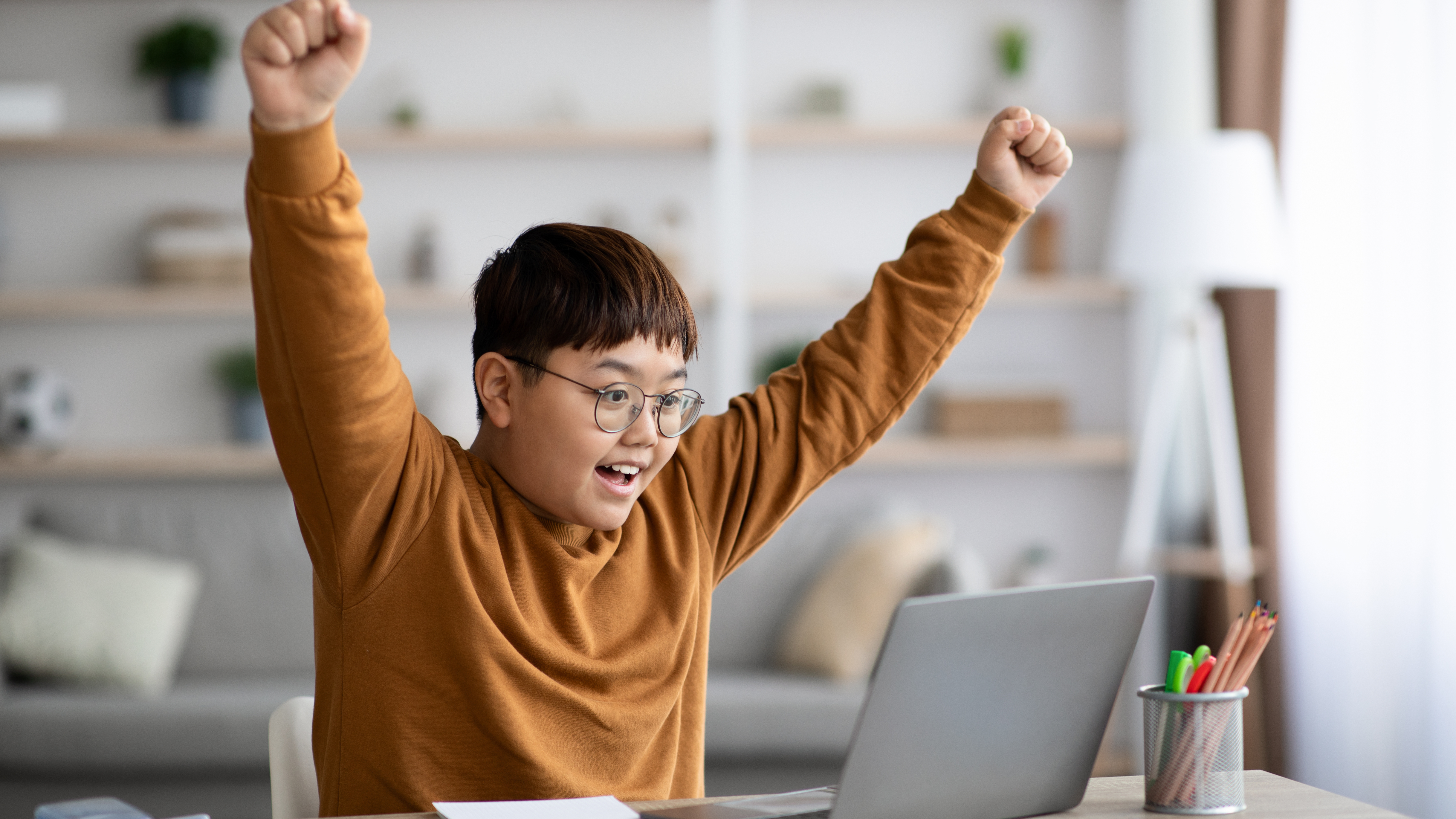 student cheering with his hands in the air in front of laptop