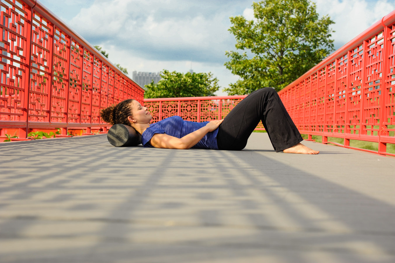 Red bridge and woman wearing a blue top laying back of neck on a foam roller