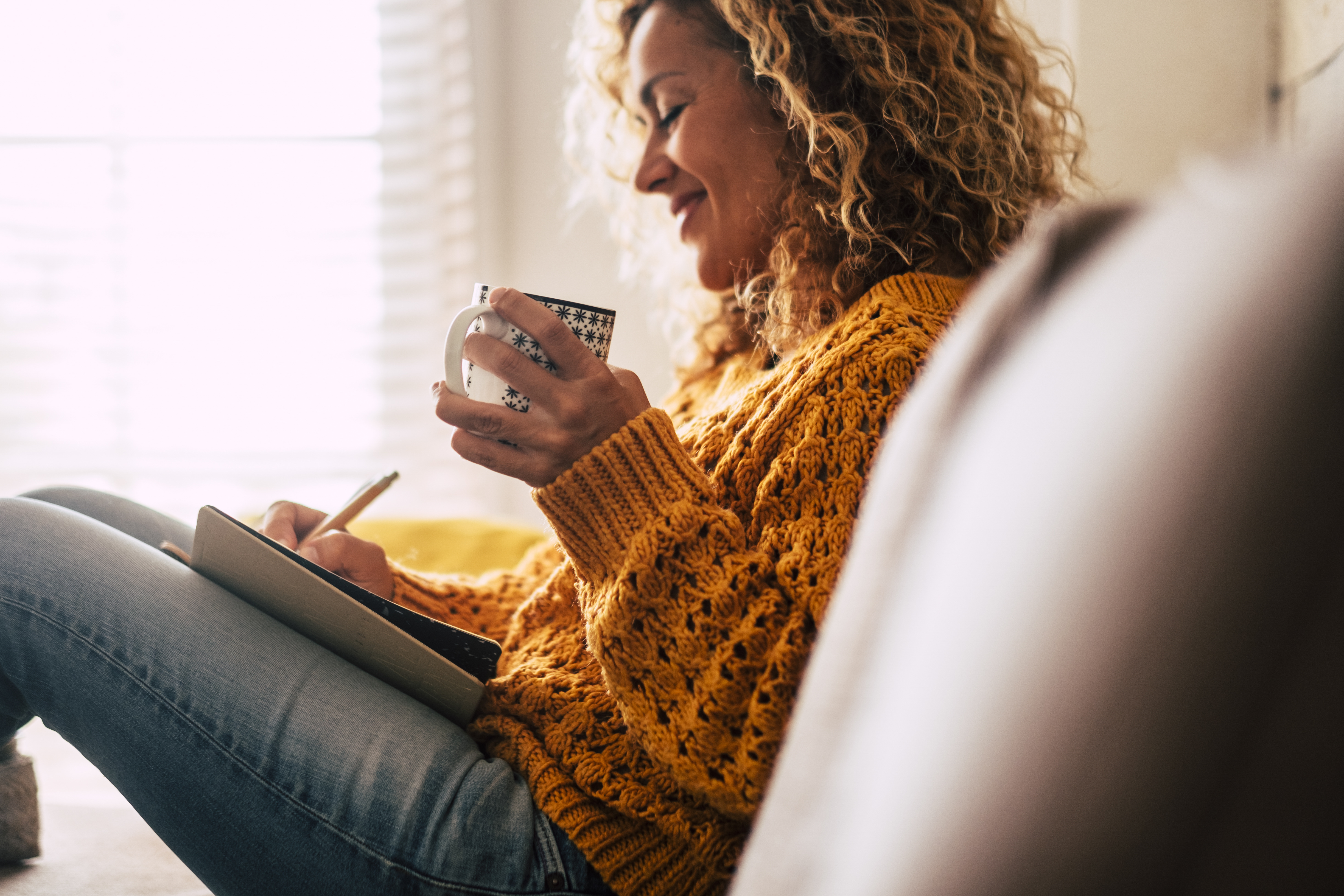 Woman on a chair drinking tea and writing into a journal