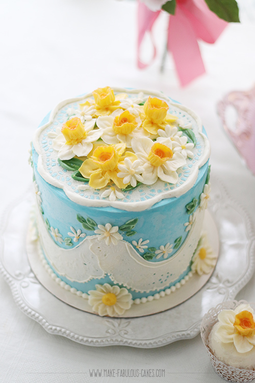 blue buttercream cake with doily and daisies and daffodils