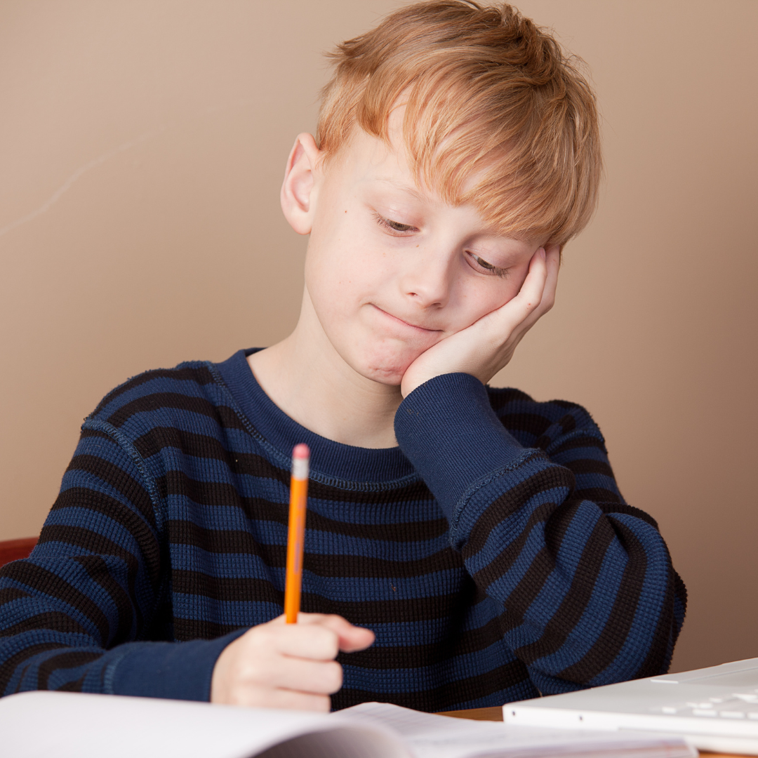 A young boy holds a pencil and reads from a school book.