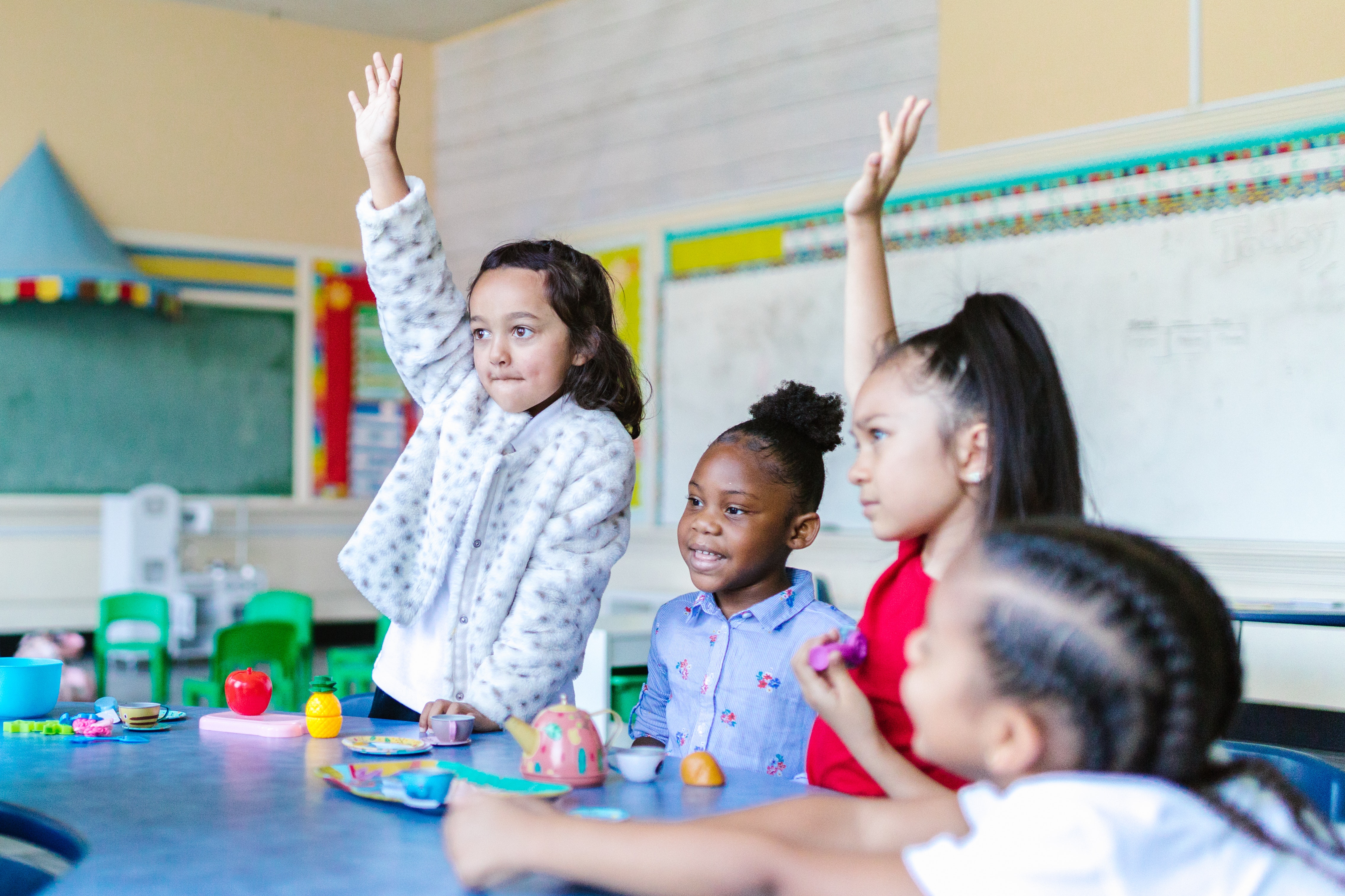 kids raising hands at table