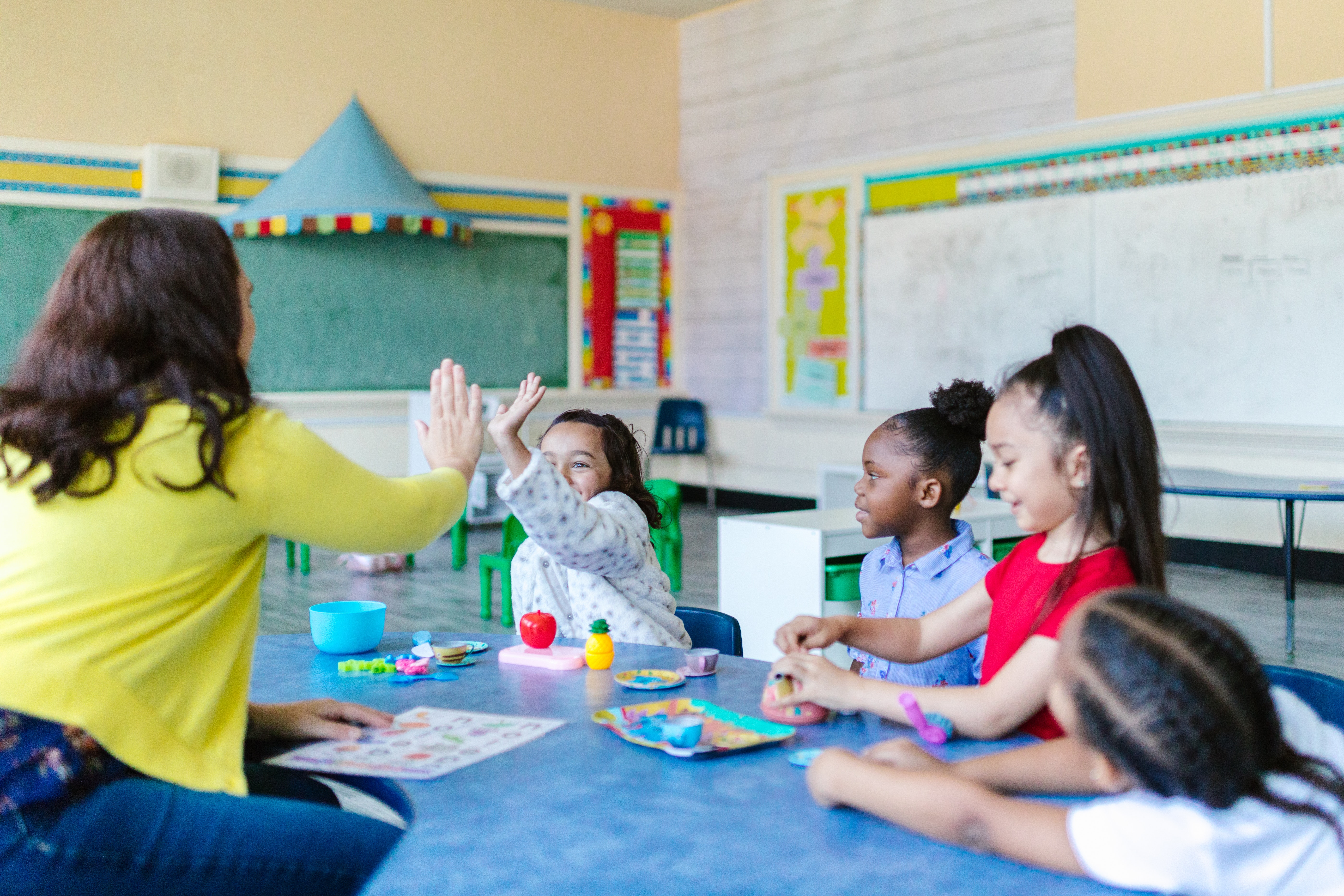 teacher high fiving student at table with other students