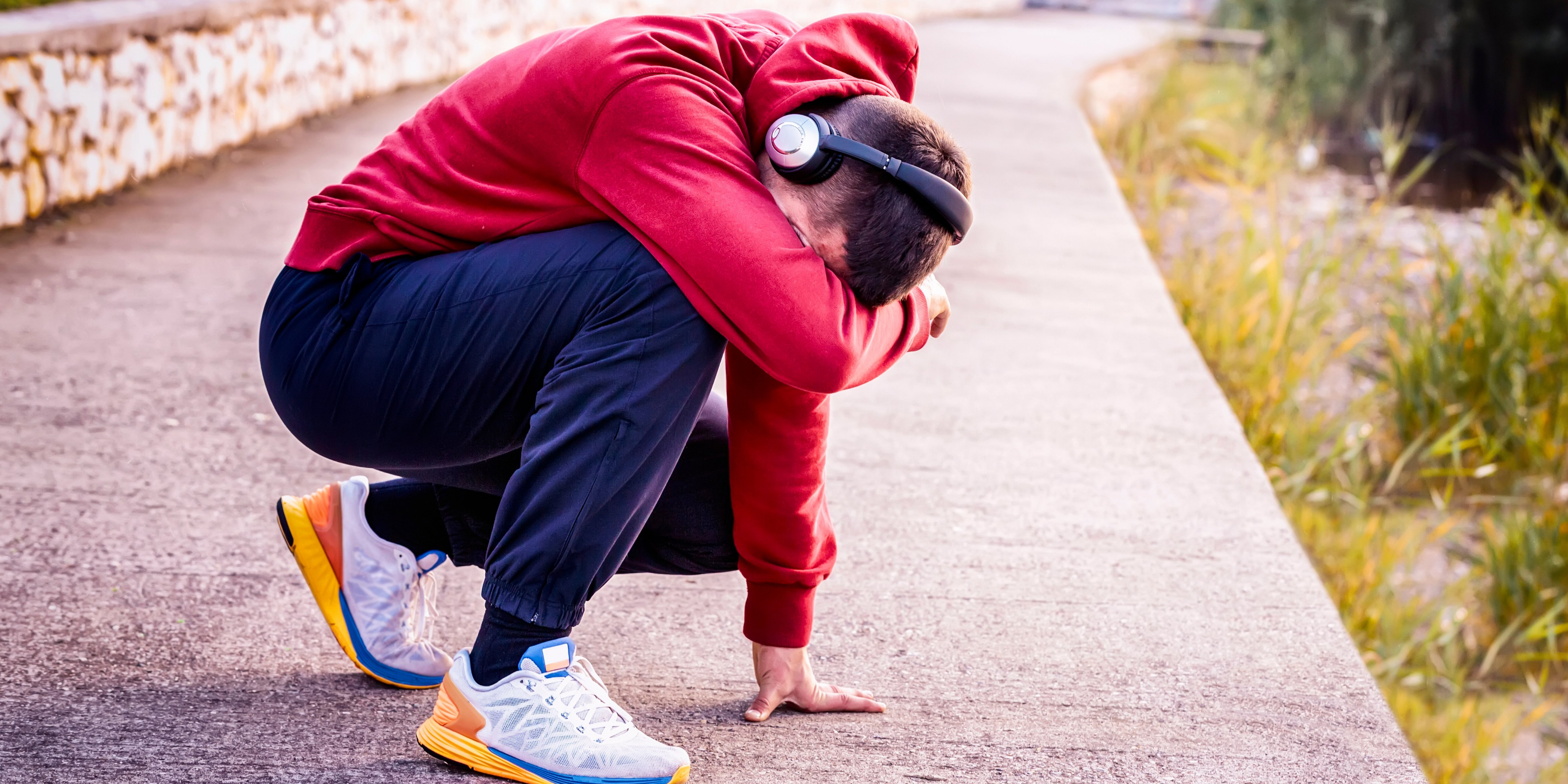 Athlete wearing a red hoodie and headset bending down due to fatigue.