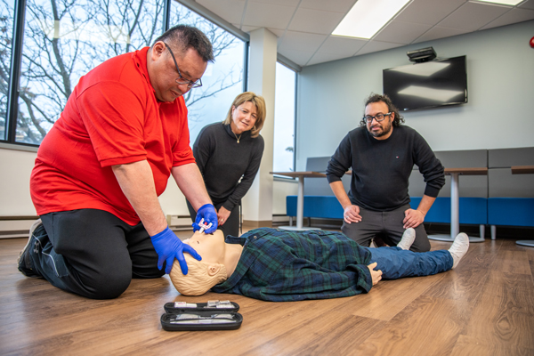 Un moniteur de la Croix‑Rouge canadienne montre comment administrer de la naloxone par voie nasale à un mannequin couché sur le sol pendant que deux apprenants observent la démonstration.