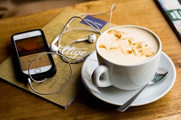 Cup of coffee with a smartphone and headphones next to it