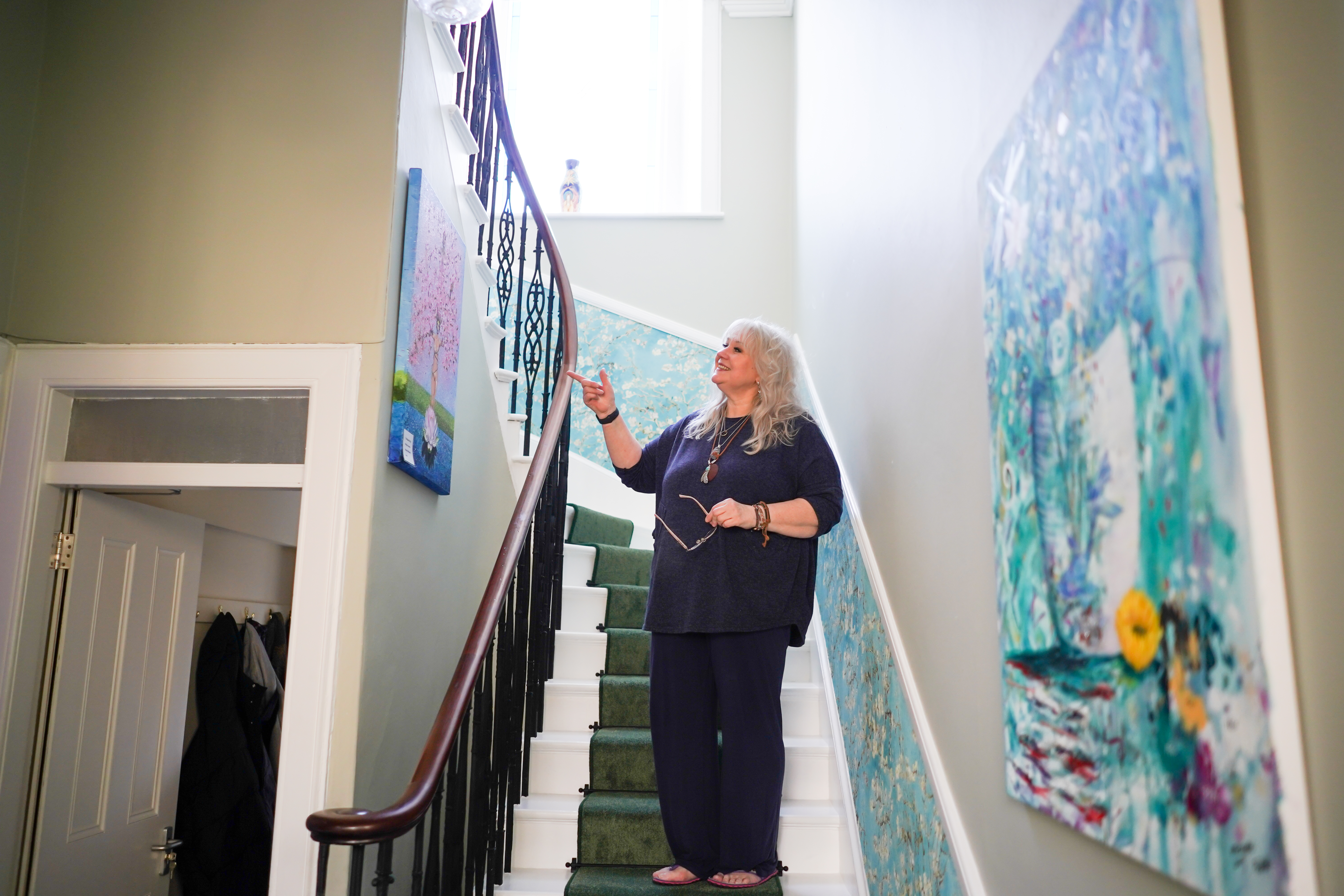 Pic of a woman standing on a stairway pointing at a painting