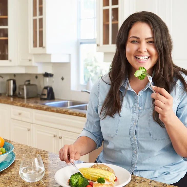 smiling woman in kitchen eating healthy food