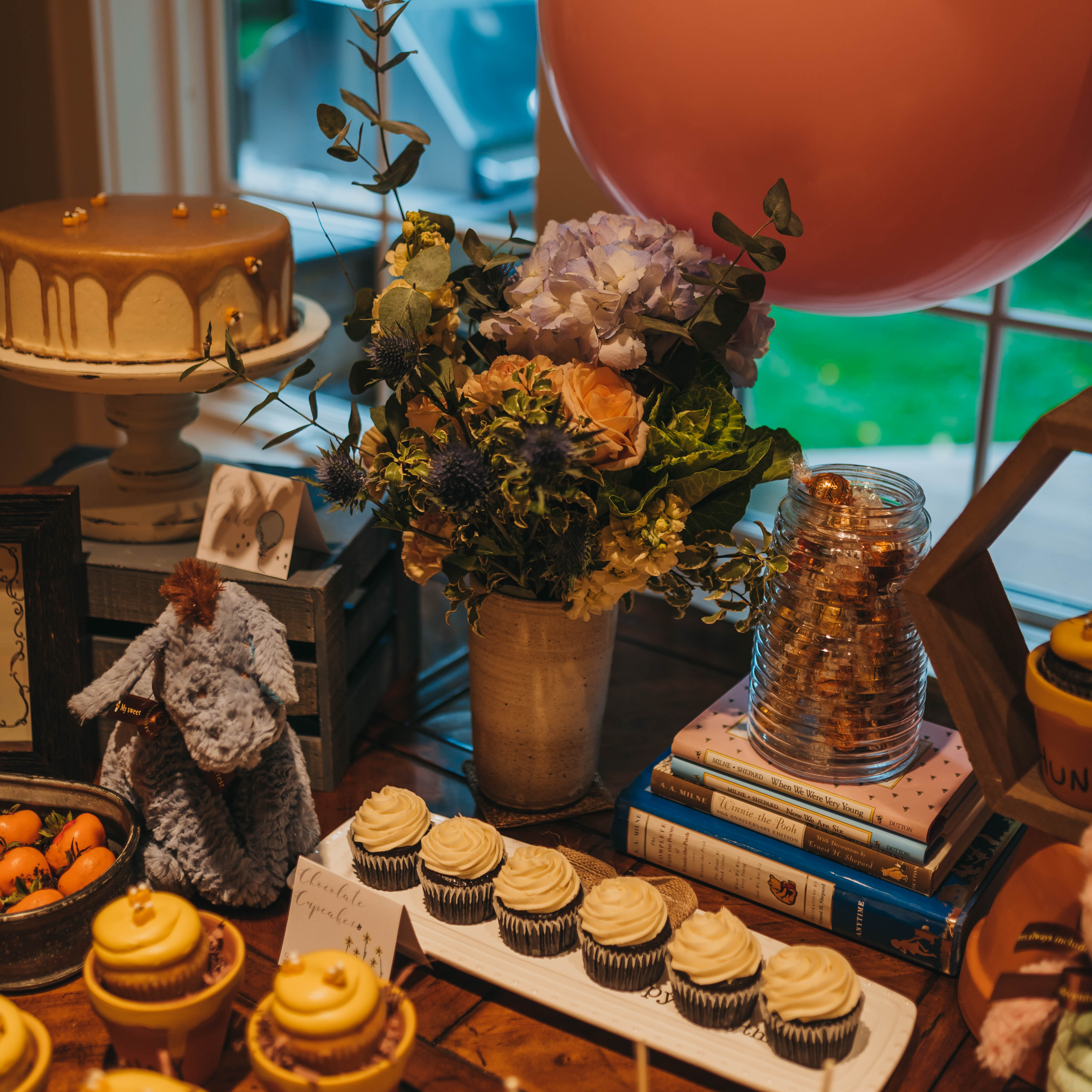 Winnie The Pooh themed tablescape with honey cake, yellow frosted cupcakes, plants, and balloons