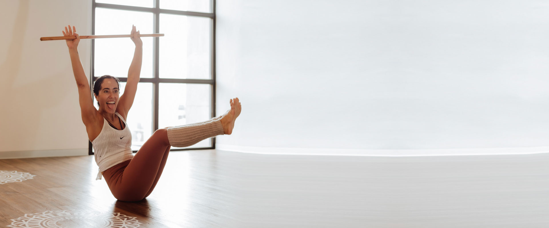 Mujer saca la lengua mientras practica yoga en una postura de bote en una studio de yoga.