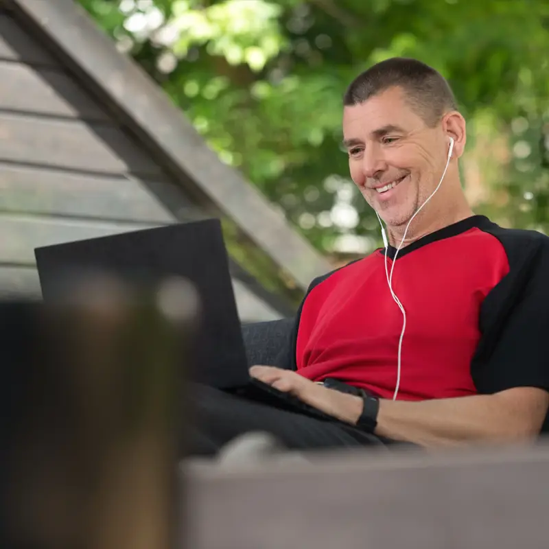 A person wearing headphones is actively taking a Red Cross course on their laptop while sitting on their patio.