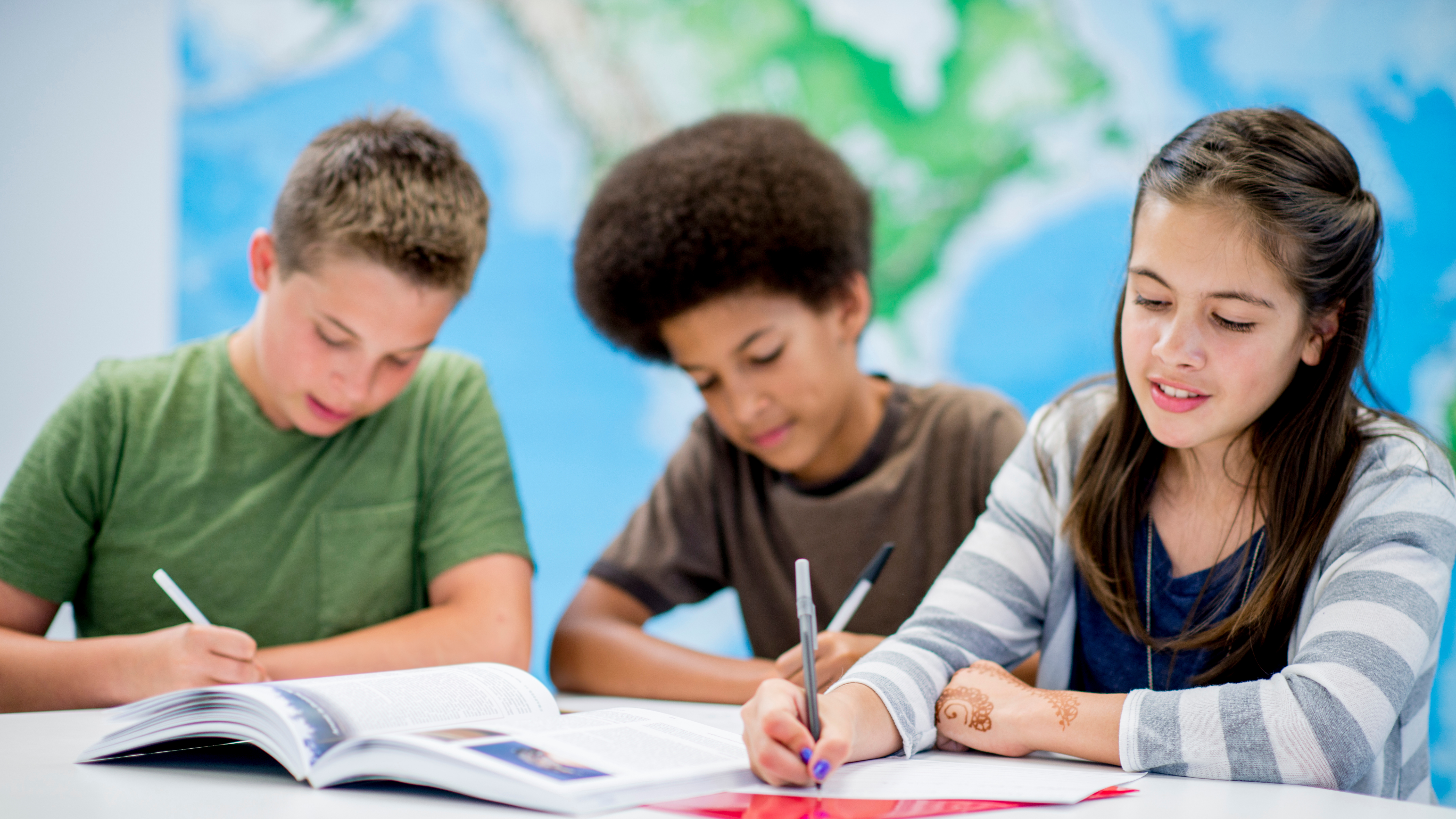 three students writing at a table together