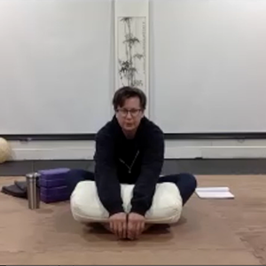 Seated yoga instructor holding a white bolster on her lap.