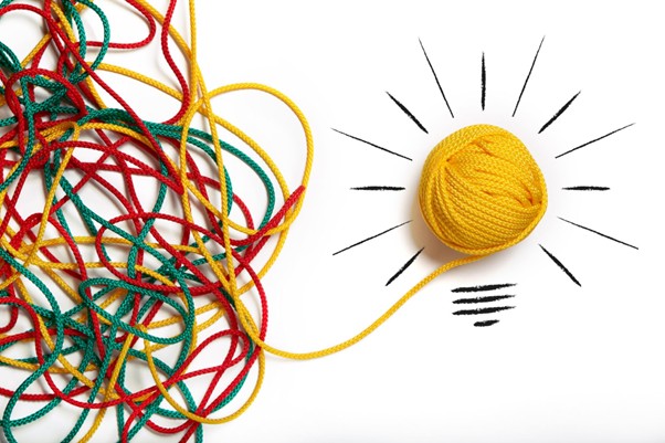 Lots of strands of different coloured string coming together in the form of a ball that has artistic lines drawn around it to create a lightbul