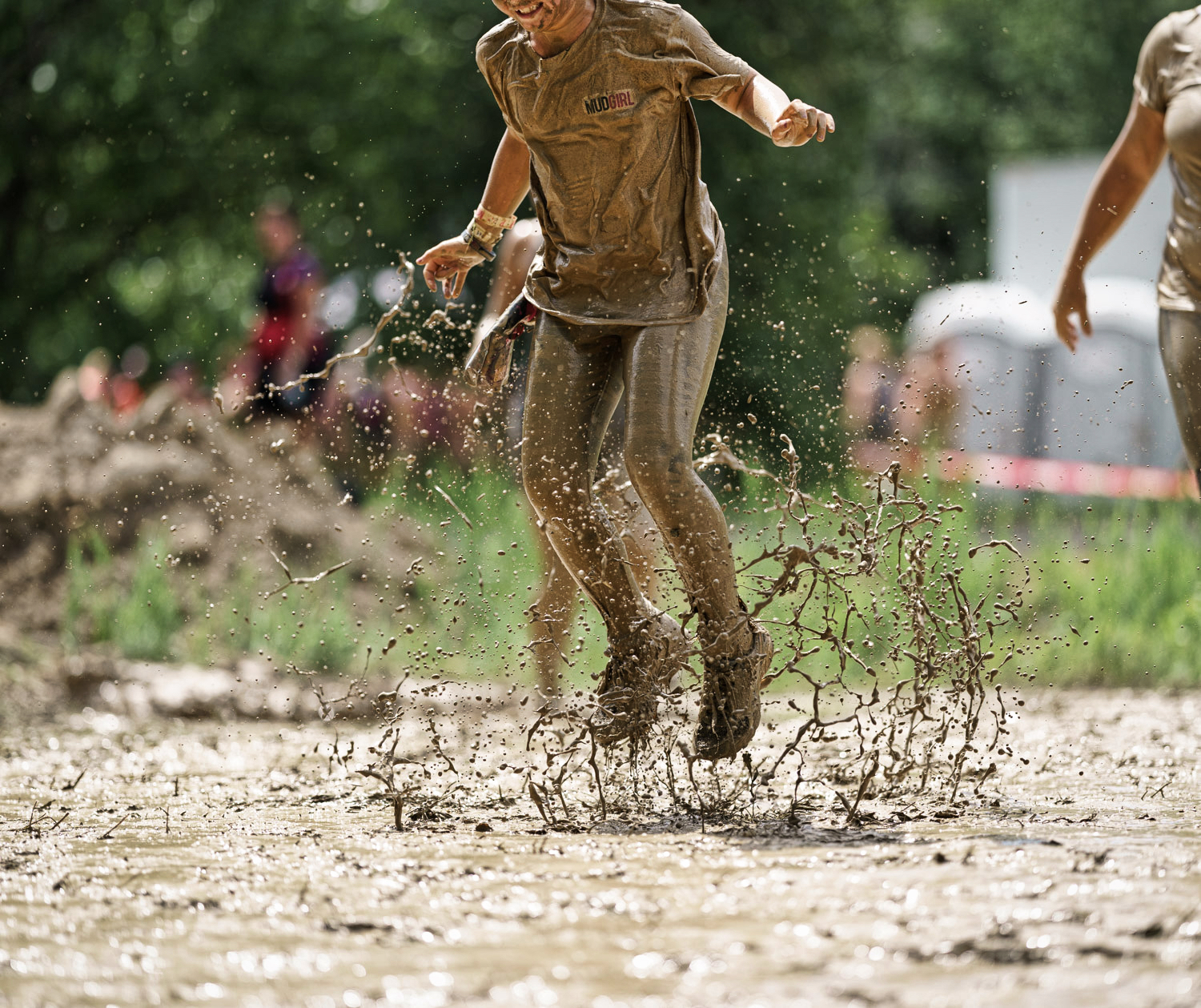 Photo d&#39;une jeune femme qui saute dans la boue. Le mouvement de la boue est figé dans les airs.