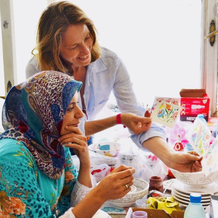 Photo of Mimi Robinson showing a painting to an artisan