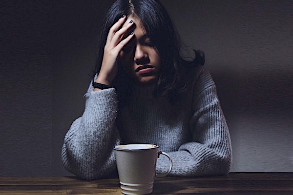 Young woman looking exhausted with a drink in a mug in front of her