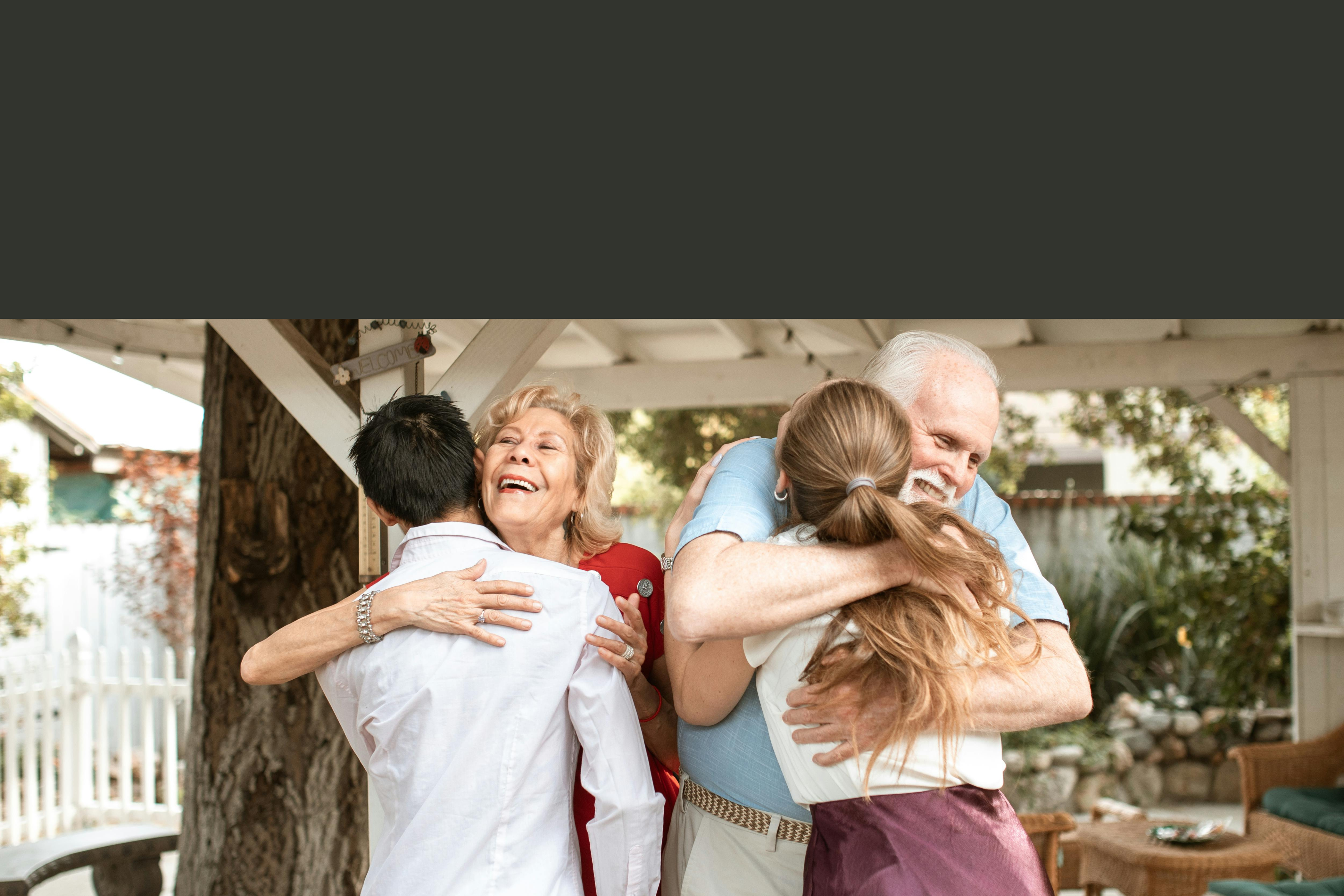 Elderly couple hugging younger couple by welcome sign