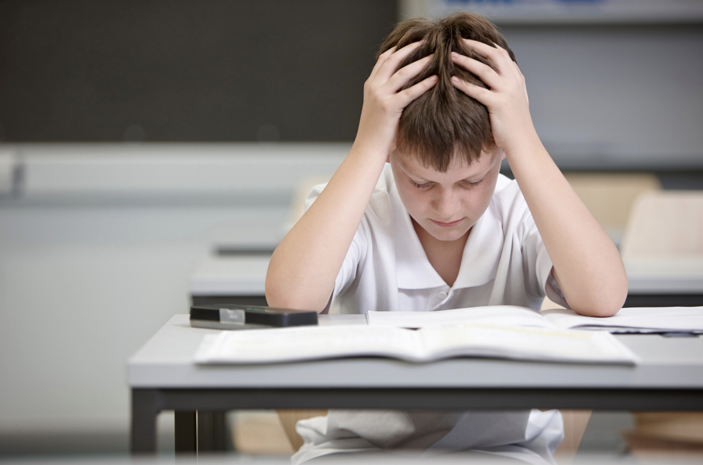 a young boy stares at homework with his hands on his head.