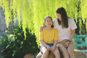 Mom and daughter sitting outside on a rock under a tree