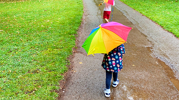 Two children with rainbow umbrellas on a rainy path