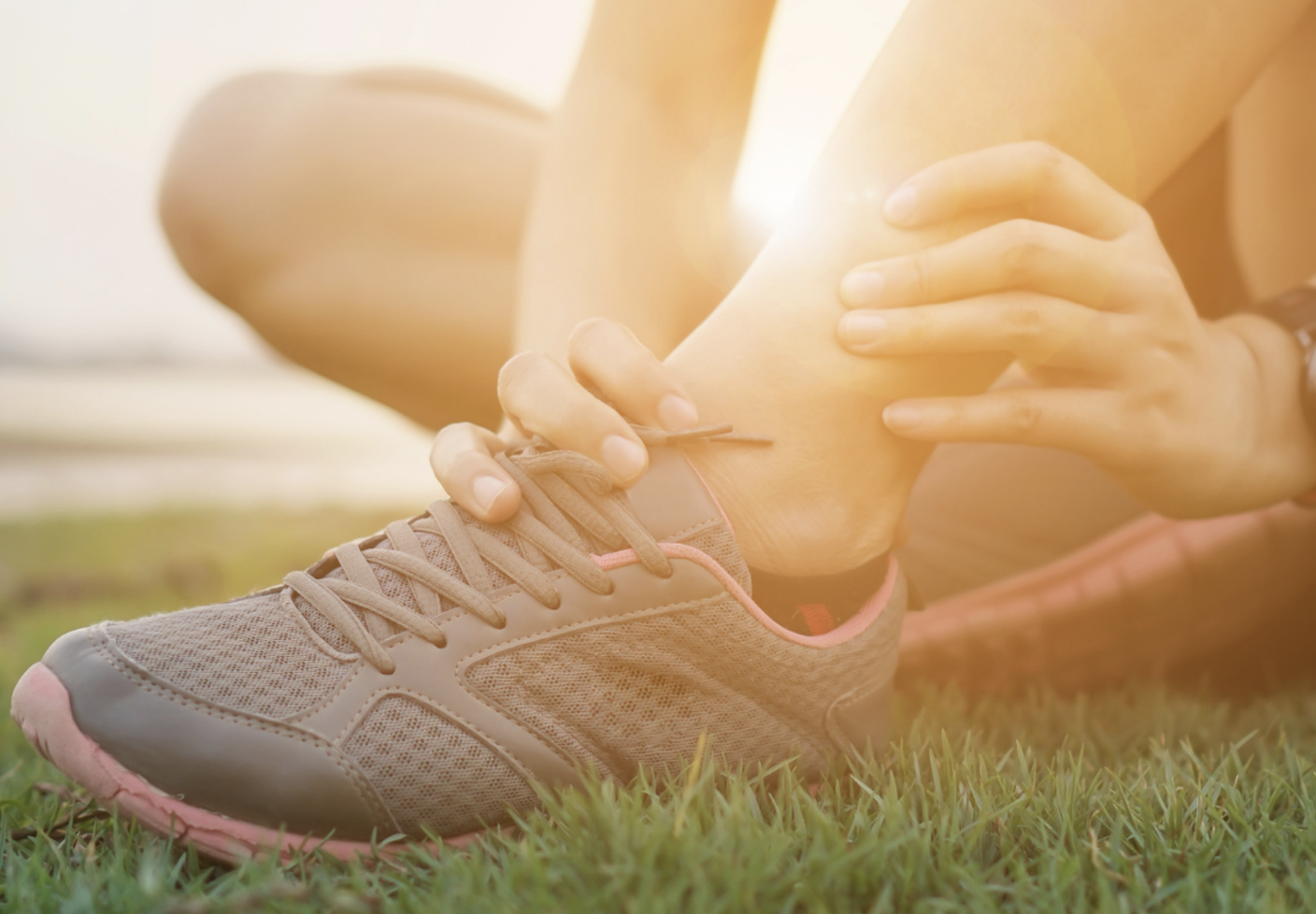 Woman holding her ankle due to ankle pain from lower limb injury.