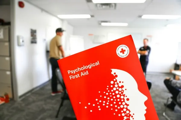 Psychological First Aid booklet by the Canadian Red Cross and at the background a classroom with students. 