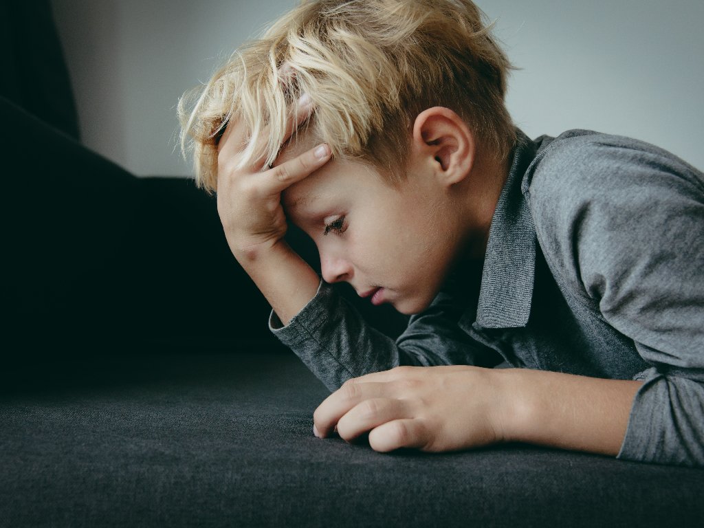 little boy holding his head and looking sad