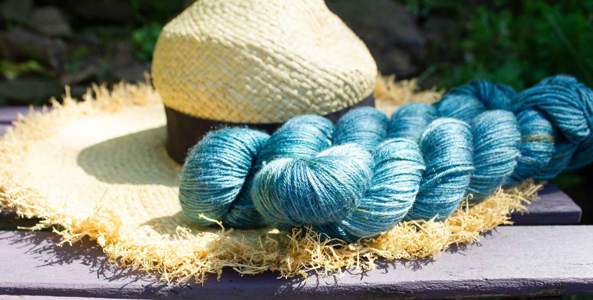 Skein of bright blue yarn lying on a sun hat outside in a garden.