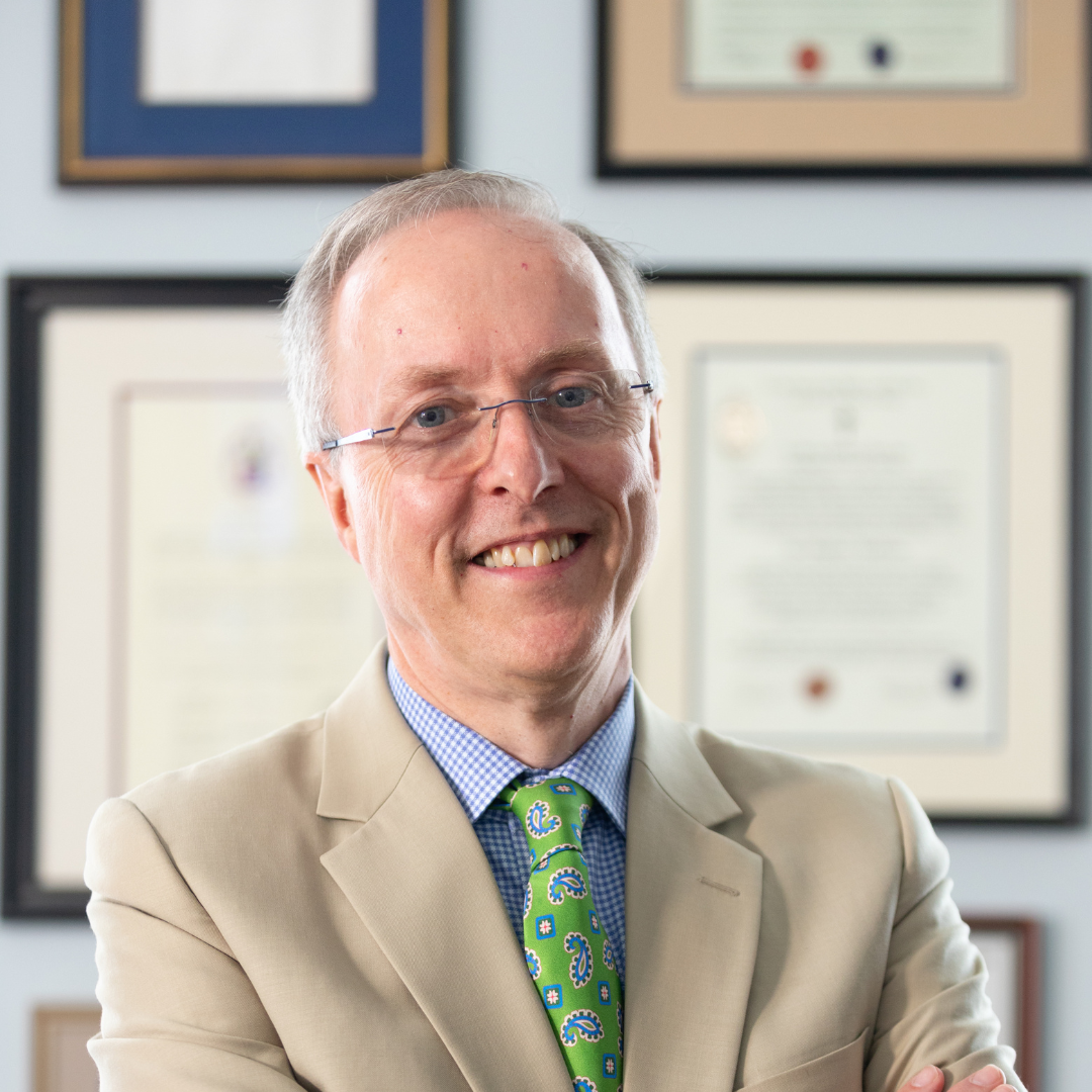 Man in a beige suit with a green tie and glasses.