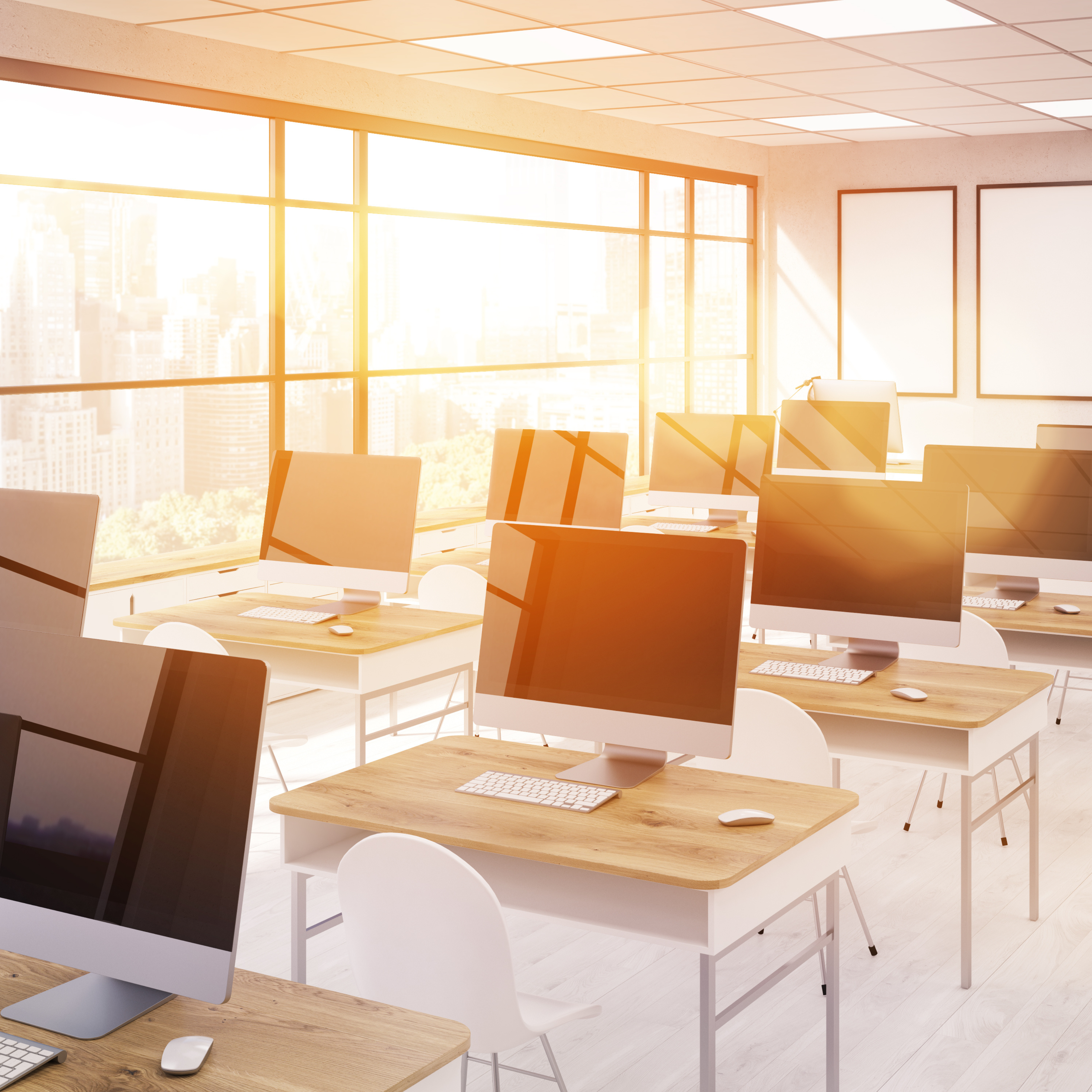 a classroom with desks that have desktop computers, sun shining in the room