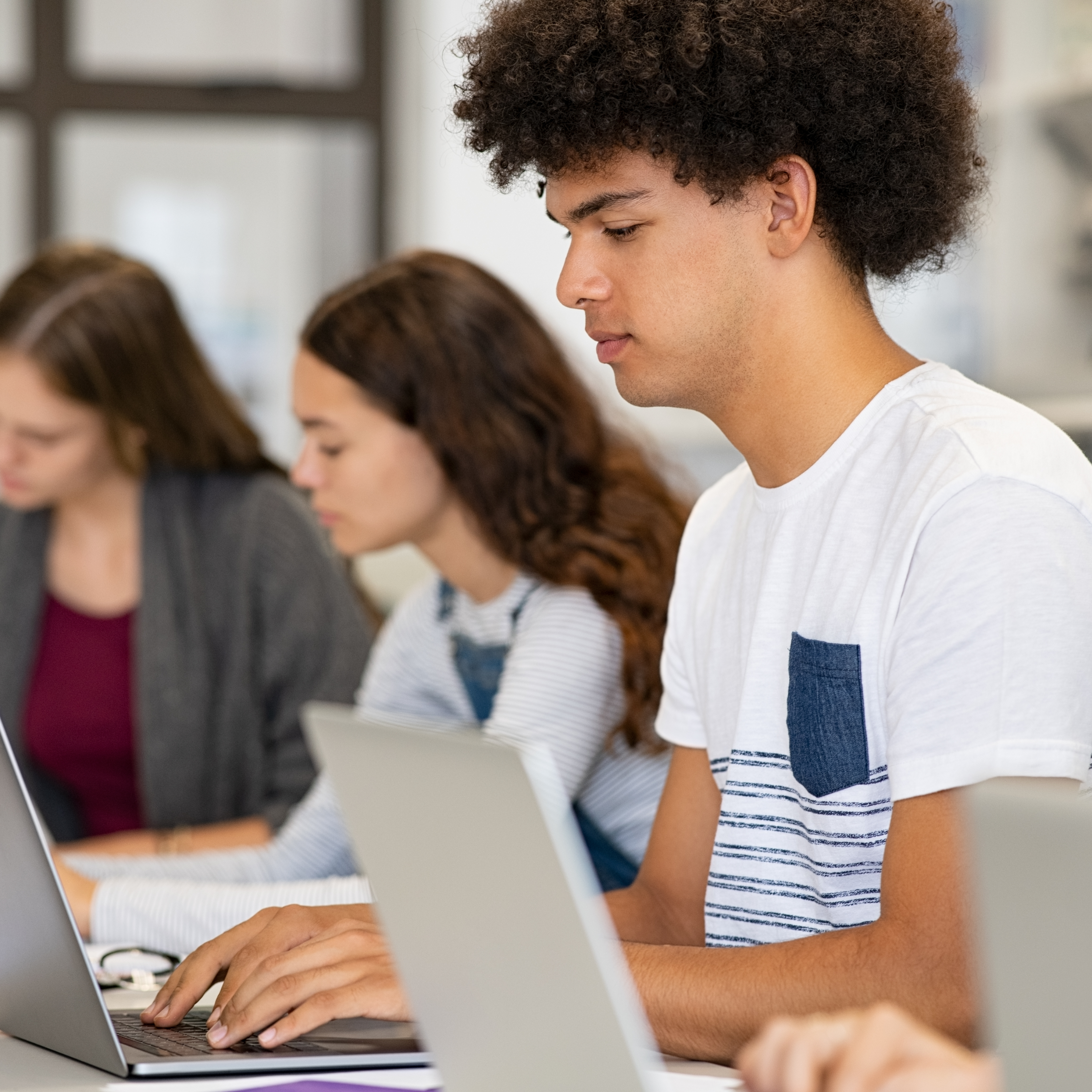 student working on a laptop with peers by his side also working on laptops