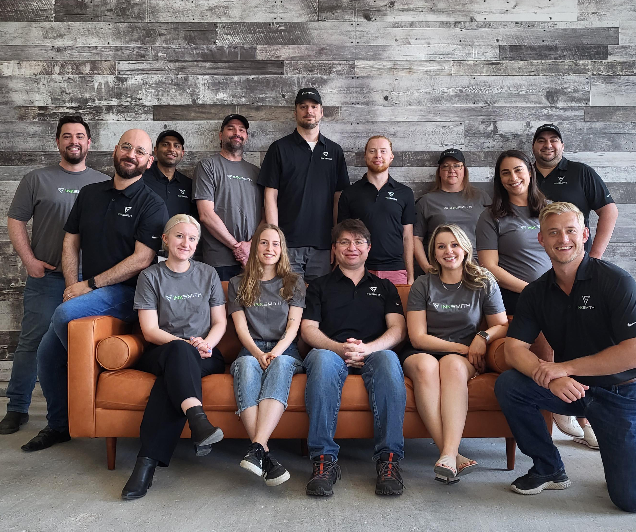 Team of 14 sitting and standing on or around a couch.