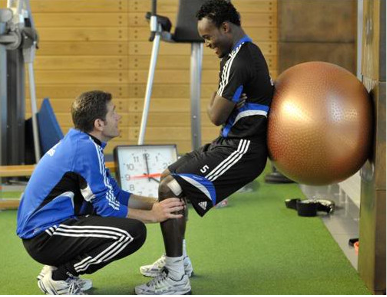 Instructor helps athlete with ACL recovery with yoga ball exercises.