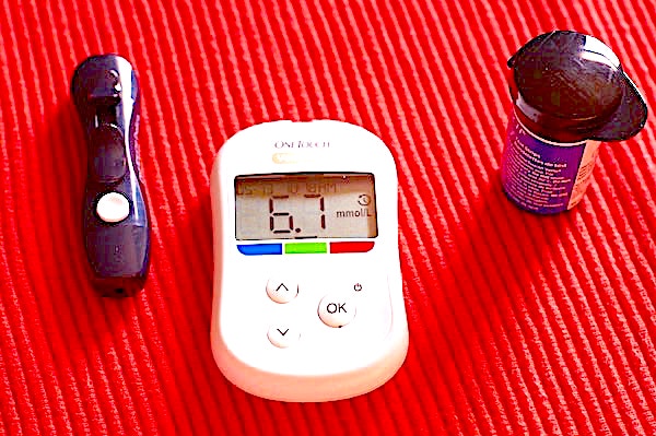 A diabetic&#39;s meter for reading blood glucose levels with lancet and plastic container for fresh test strips next to it