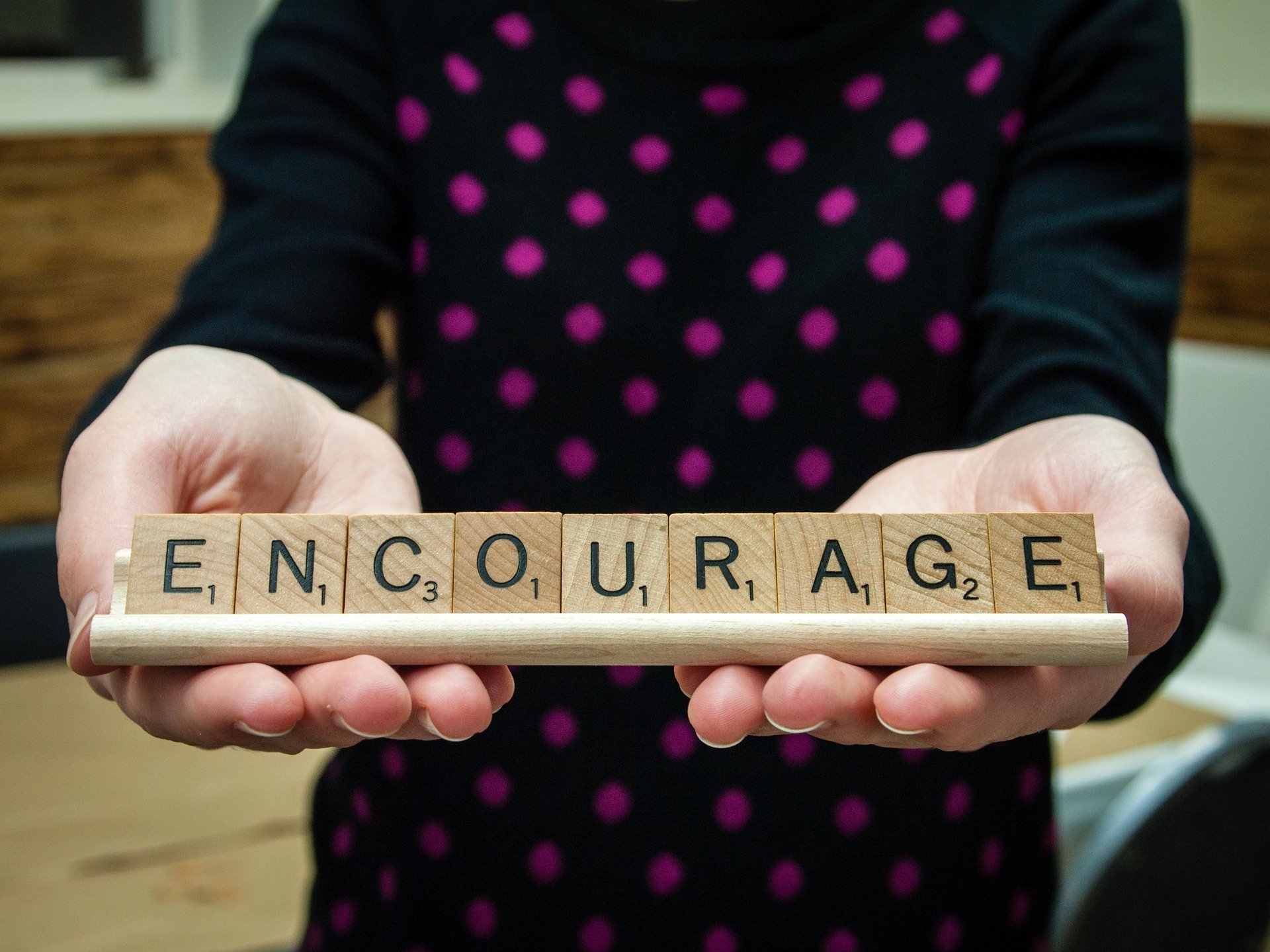 a person holding the word ENCOURAGE on wooden scrabble tiles