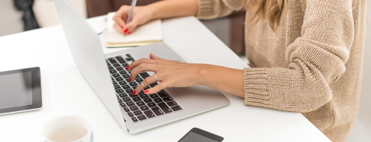 woman writing on paper and typing on laptop freelancer